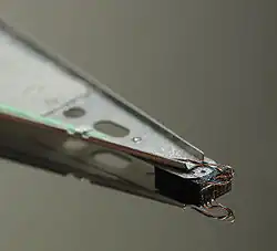 Close-up of an HDD head resting on a disk platter; its mirror reflection is visible on the platter surface. Unless the head is on a landing zone, the heads touching the platters while in operation can be catastrophic.