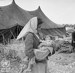 A Palestine refugee girl carries her sleeping baby sister in the newly formed Mia Mia camp, 1949.
