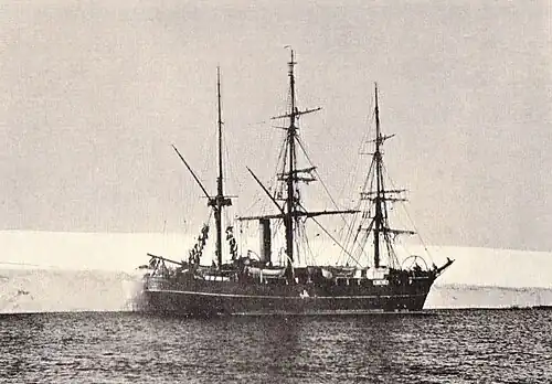 Three-masted ship with sails furled, lying next to a shelf of ice.