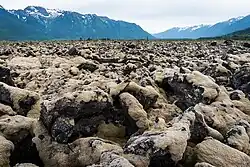 Jagged, moss-covered rocks in a valley bounded by lightly snow-covered mountains