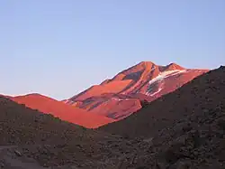 A mountain glows red above a shaded valley