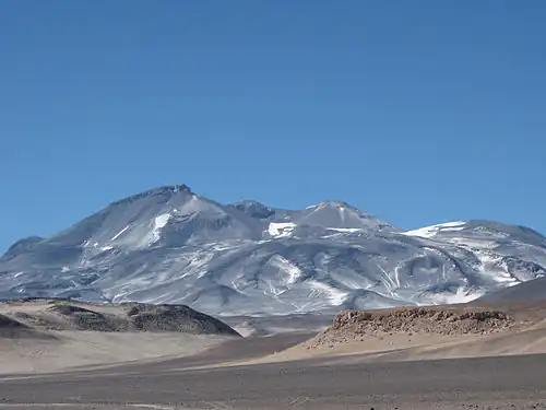 Photo: A broad, irregular mountain in an unvegetated landscape with sparse snowpatches
