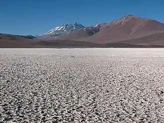 Mountains, including a snow-covered one in the middle, rise above a rough white surface