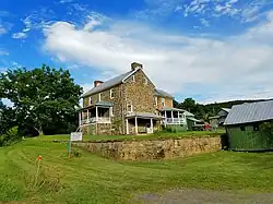 Two story stone house as seen from across a grassy yard, with a stone wall and historical marker in the foreground