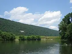 An image of a river in the foreground and a forested mountain ridge in the background, topped with a blue sky and clouds