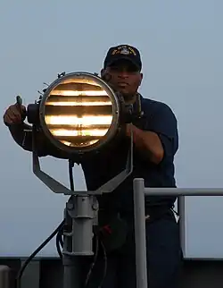 US Navy sailor sending Morse code using a signal lamp.
