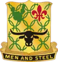 A Gold color metal and enamel device 1+1⁄8 inches (2.9 cm) in height overall consisting of a shield blazoned: Or, chain mail Vert, in chief a prickly pear cactus of the last and a fleur-de-lis Gules and in base a carabao affronté Sable. Attached below and to the sides of the shield a Black scroll turned Gold inscribed "MEN AND STEEL" in Gold letters.