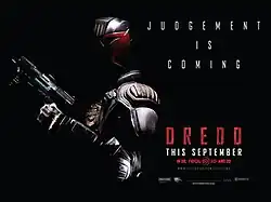 A futuristic police officer in armour and a helmet that covers all but his mouth stands on the corner of a building roof with a gun in his hand as large tower blocks burn behind him. Above the man reads a tagline "Judgment Is Coming".