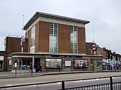 A brown-bricked building with a rectangular, dark blue sign reading "RAYNERS LANE STATION" in white letters all under a dark blue sky
