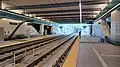 The below ground Spring District station on opening weekend in April 2024. The station has a high ceiling with exposed beams and bright lights. The station has two platforms on the sides of the station with two tracks running down the center. There are benches along the platform for passengers to wait. The walls are decorated with artwork, and there are signs with information about the station and train schedules.